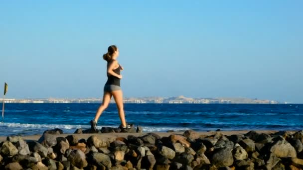 Sports girl running along the stone path to the sea. Brunette looks away and dreams. — Stock Video