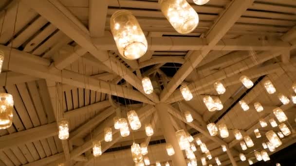 Self-made lanterns from cans are suspended on a wooden ceiling and shine brightly. Camera moves around the fixtures and the ceiling fan. — Stock Video