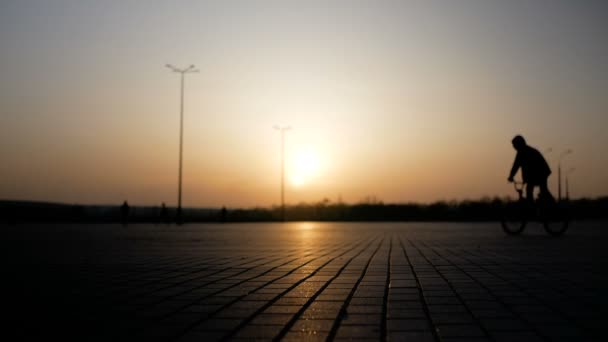 Ragazzi andare in bicicletta verso il tramonto su una vasta area. Silhouette persone sullo sfondo del sole . — Video Stock