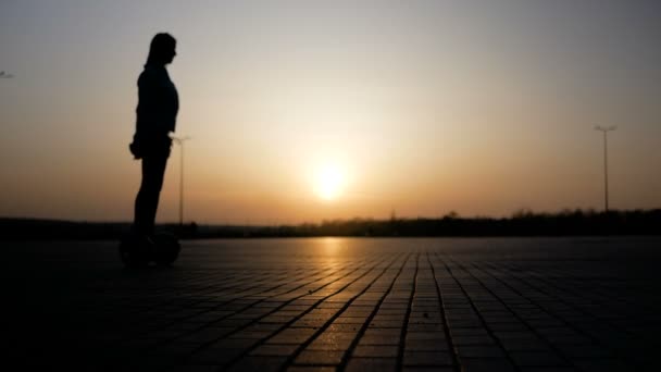 Het meisje is rijden door op de segway tegen de achtergrond van de zonsondergang, en een jonge man loopt door haar. — Stockvideo