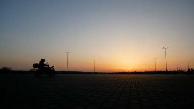 Motorcu güzel bir gün batımı zemin karşı büyük bir kare üzerinde quad bisiklet sürmek.