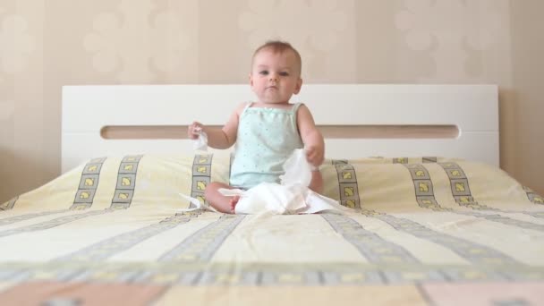 Baby is playing with white napkins while sitting on the bed. Emotional kid. The first joy is simple things. — Stock Video