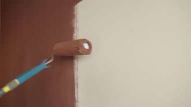 Boya silindiri. Beyaz, çıplak bir duvarı yukarı aşağı fırçalamak. Kahverengi renk. Tasarım konsepti. Sapı yakın çekim ve sağ taraftan bir el..