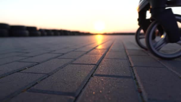 Makroaufnahme von Kinderwagenrädern und Mütterschuhen. Sonnenuntergang und Horizonlinie im Hintergrund. — Stockvideo
