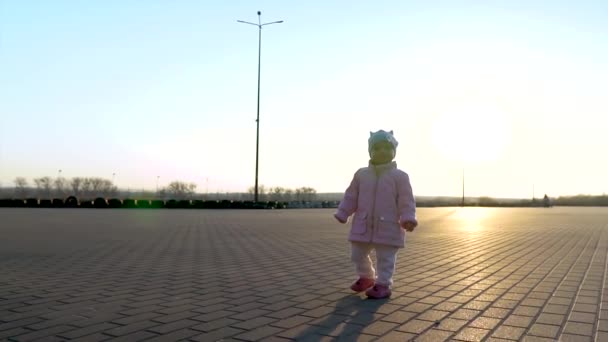 Slow mo of baby walking and staying in the empty square. Sunset behind. Sunrays and blue sky. Leisure time. — Stock Video