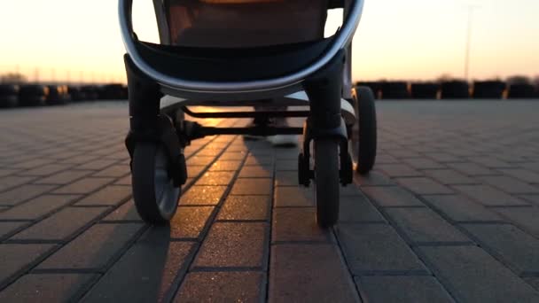 Närbild av barnvagnshjul medan mamma går. Solnedgång, solstrålar och skuggor. — Stockvideo