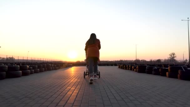 Zadní a postranní záběr, jak máma běží s kočárkem. Cesta k chodníku. Západ slunce. — Stock video