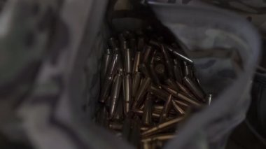 Kamuflaj çantasında bir sürü mermi var. Bir asker saldırı tüfeği şarjörü dolduruyor. Askeri malzeme..
