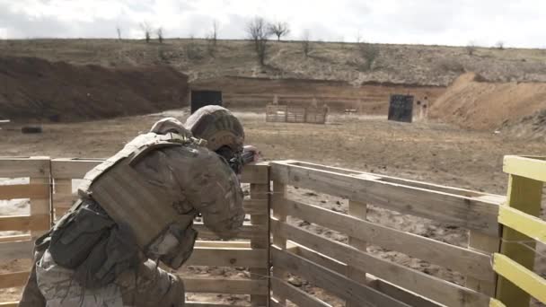Um novato totalmente equipado em uma camuflagem dispara de um rifle de assalto no campo de treinamento ao ar livre. Um tiro pelas costas. Dia ensolarado . — Vídeo de Stock