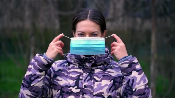 Młoda kobieta zakłada maskę medyczną i patrzy w kamerę. Oddalenie się od społeczeństwa. Opieka zdrowotna i koncepcja medyczna. — Wideo stockowe