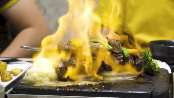 Close up beef meat on hot dish on fire with vegetables in slow motion. Live cooking in the restaurant. — Stock Video