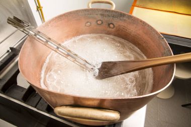 termometre ve büyük kaşık ile bakır tavada şeker şurubu kaynar