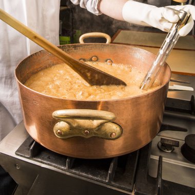 termometre ve büyük kaşık ile bakır tavada şeker şurubu kaynar. Kahverengi renk buharlaşma nedeniyle.