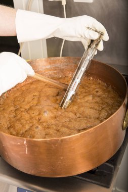 termometre ve büyük kaşık ile bakır tavada şeker şurubu kaynar. Kahverengi renk buharlaşma nedeniyle.