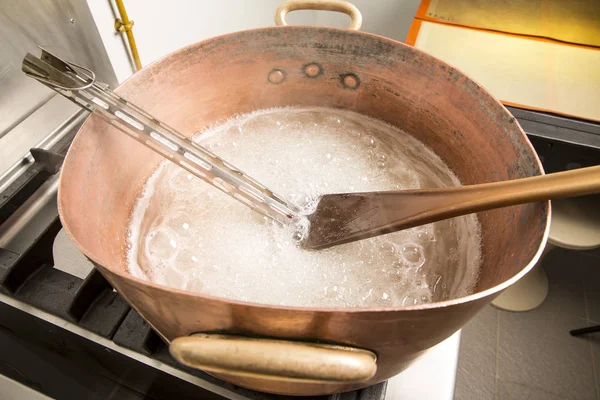 termometre ve büyük kaşık ile bakır tavada şeker şurubu kaynar