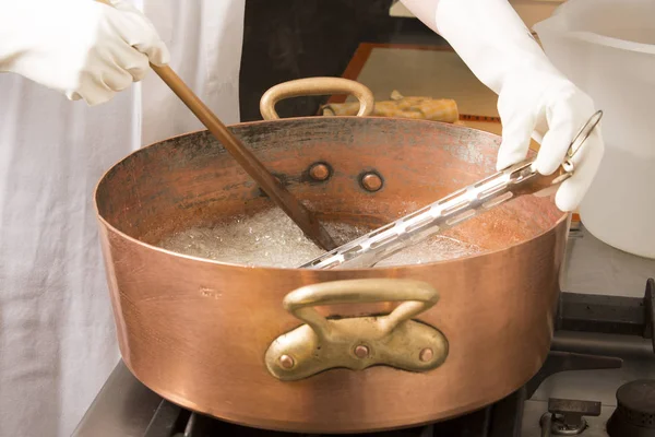 termometre ve büyük kaşık ile bakır tavada şeker şurubu kaynar