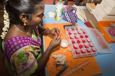 Belgesel yayın. Yaklaşık, Puduchery, Pondichery, Tamil Nadu, Hindistan - 2018 Mart. Kimliği belirsiz kadın kadın sanatçı el ile jewelleries kağıt olun. Küpe, kolye, çiçek. Kağıt geri dönüşüm ile.