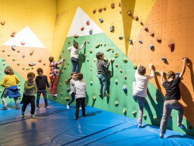 Genç sporcu kadınlar ve okul çocukları duvarlara tırmanırken küçük kayaları tutuyorlar.