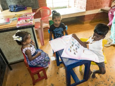 Sevimli zavallı küçük çocuk, erkek kızlar, masada sandalyede oturan, kitap okumaya çalışıyor