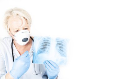 Mature caucasian european doctor with blond hair and anxious behaviour, wearing a face FFP2 mask to protect herself from covid-19 infection. With stethoscope, syringe and radiology, x-ray image of lungs clipart