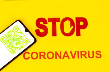 Coronavirus Covid-19 enfeksiyonu için akıllı telefon ekranında yeşil QR kodu olan Dur İşareti işçilerin sağlık virüsü enfeksiyonunu öğrenmesi için kullanılıyor. Sarı arka plan. Dünyada salgın virüse karşı yeni bir yol