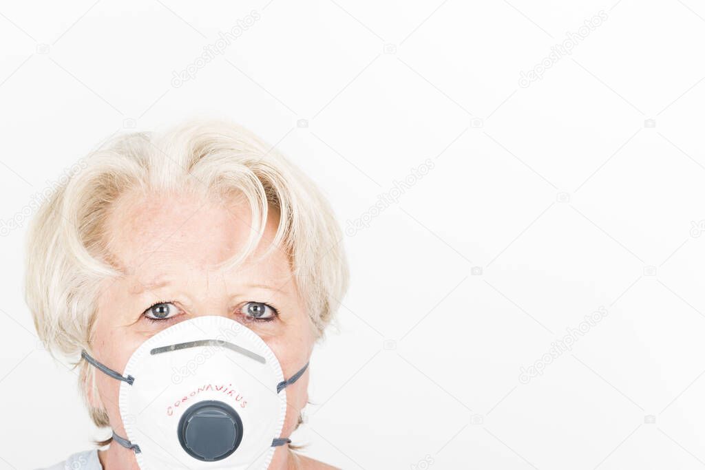 Close-up of a mature caucasian european woman with blond hair and anxious behaviour, wearing a face FFP2 mask to protect herself from covid-19 infection or air pollution.