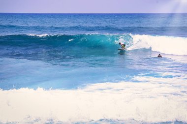 Hossegor, Fransa - Şubat 2019. Kimliği belirsiz bir sörfçü kıyıya yakın bir okyanus dalgasında, mavi okyanusta iyi bir altın ışıkla at sürüyor..