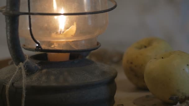 Lámpara antigua con vela en una mesa de madera con manzanas en la noche, el agricultor trajo una lámpara, una linterna, iluminó la habitación 4K — Vídeos de Stock