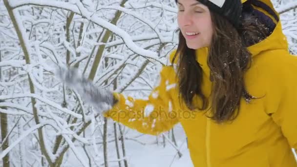 Ő megy, és lerázza a fenyő ágak hóval borított a hó a télen. Mosolygó és boldog télen — Stock videók