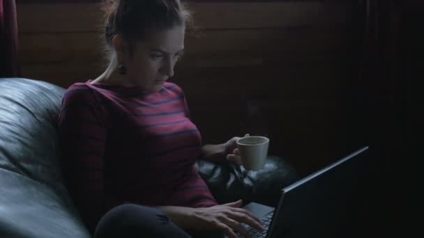 Meisje zittend in een stoel met laptop en het drinken van thee. Is thuiswerken. — Stockvideo