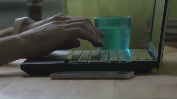 Homem está digitando no laptop com um copo de água — Vídeo de Stock
