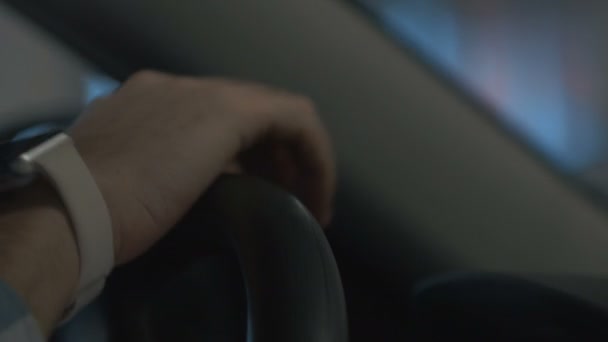 Male hand operates steering wheel of moving vehicle in city lights at night. Right side view — Stock Video