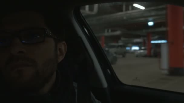 地下駐車場で車を運転する男。クローズ アップ。背景のボケ味 — ストック動画