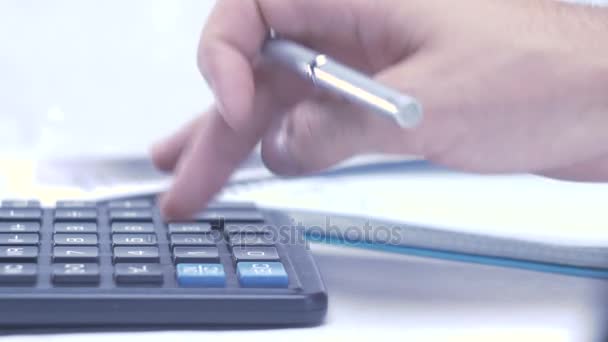O homem considera na calculadora e fazendo anotações em um caderno — Vídeo de Stock