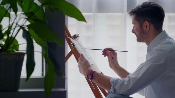 Egy férfi rajzol egy képet egy állványra a stúdiójában. — Stock videók