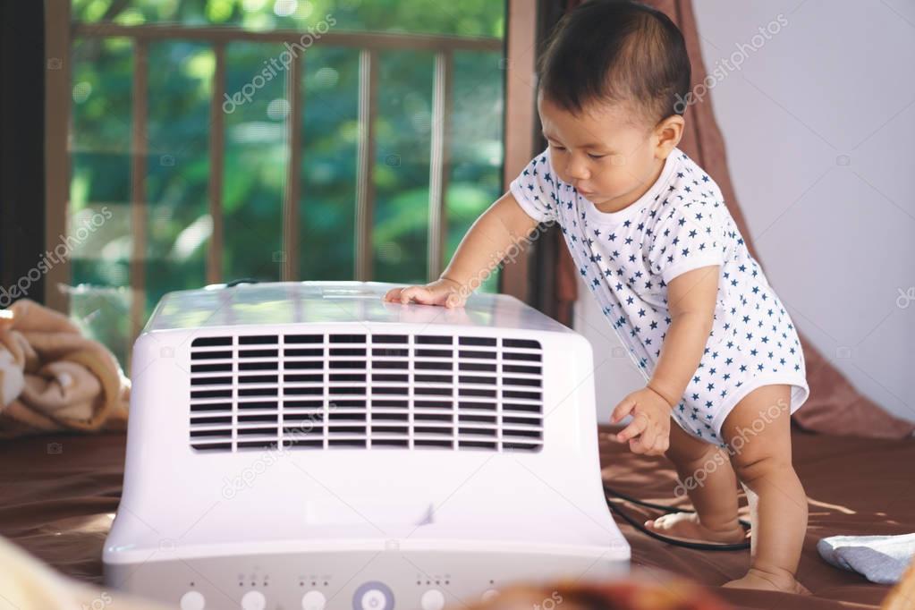 Asian baby curious looking at mobile air conditioner Stock Photo by