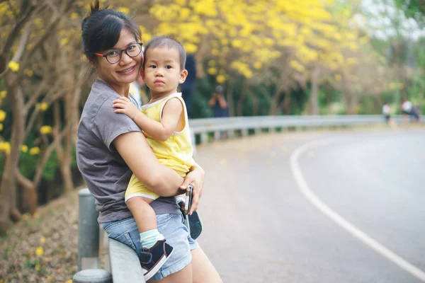 Ázsiai anya és fia, a parkban, sárga trombita virág — Stock Fotó