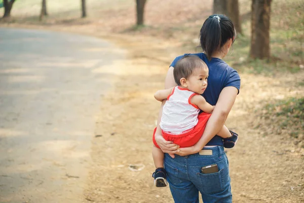 Asian mother giving her son piggyback at the park — Stock Photo, Image