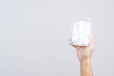 Beyaz arka planda yumuşak pamuk toplarıyla dolu plastik bir kutu.