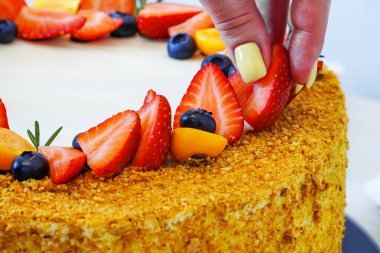 Kız taze pişmiş bir puf keki meyve ve meyvelerle süslüyor: çilek, yabanmersini ve bitki özü.                         