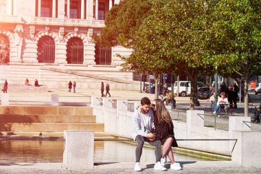 Porto, Portekiz - 26 Mart 2018: Genç çift smartphone üzerinde Internet tarama ile adam bir bankta oturmuş