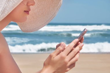Kumsalda dinlenirken cep telefonu kullanarak şapkalı güzel kadın