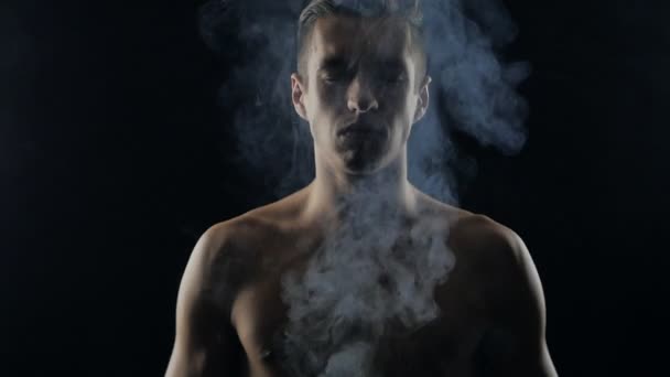 Knappe man van de shirtless en permanent op donkere achtergrond, met rook om hem heen. — Stockvideo