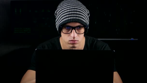 メガネと帽子の暗いオフィスの部屋のコンピューターに取り組んでいる男性のハッカー — ストック動画