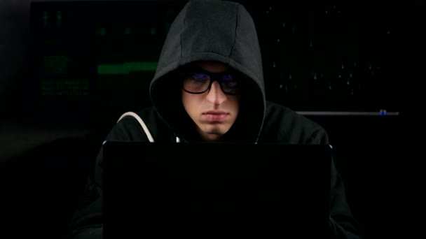 Hacker con gafas y en una encapuchada trabajando en un ordenador en un cuarto oscuro de la oficina — Vídeos de Stock