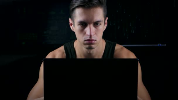 Male hacker in singlet working on a computer in a dark office room — Stock Video