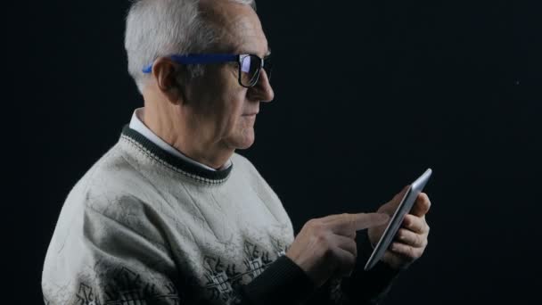 Hombre mayor con gafas trabajando en tableta digital en habitación oscura — Vídeo de stock
