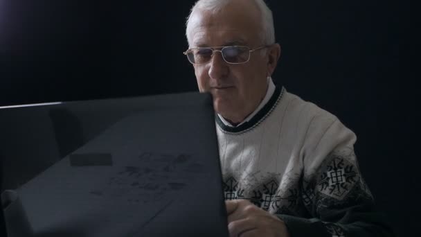 Senior man aan het werk op een laptop in de donkere kamer — Stockvideo