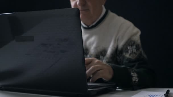 Starší muž pracuje na notebooku v temné místnosti — Stock video