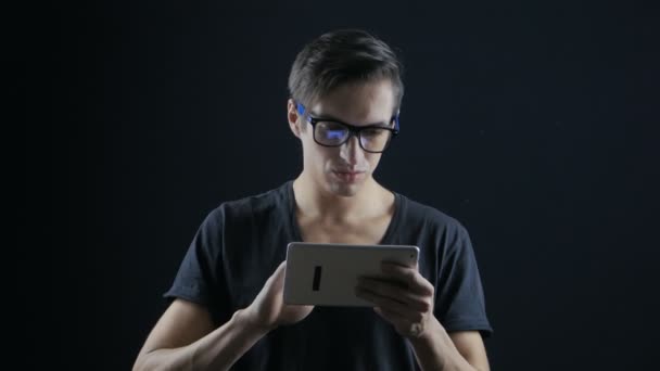 Красивый парень в очках работает над цифровым планшетом в темной комнате — стоковое видео